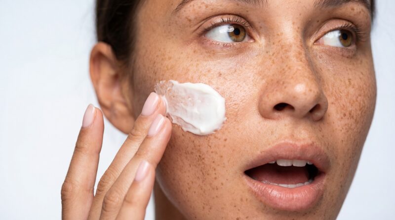 Woman with freckles applying cream on face, skincare