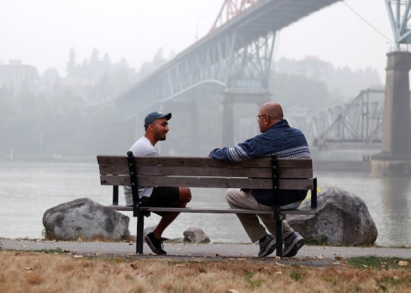 Sanga sitting on a bench near a bridge with a man