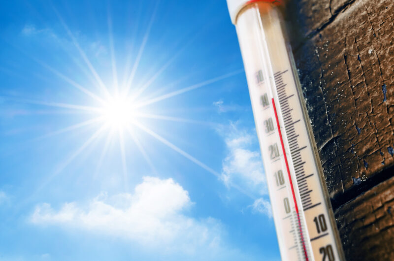 Heat Wave: Thermometer with a high temperature reading on a scale, against a background of bright sun and a blue sky with clouds. The concept of hot, dangerous weather, global warming