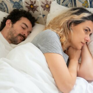 good night's sleep: woman in gray shirt lying in bed next to a sleeping man