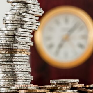 Increase your savings: stacks of coins with a wall clock in the background