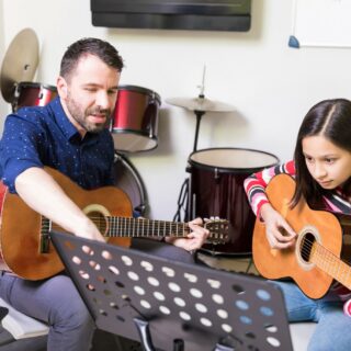 Musical Instrument: Man teaching a girl the acoustic guitar