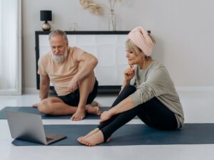 Golden Years: Man and woman sitting on yoga mats looking at a laptop