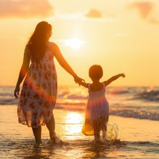 Mother's Day Gift Ideas: Mother and child walking hand in hand along the beach at sunset