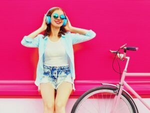 Fresh Tunes: Woman against a pink wall listening to music next to a bicycle