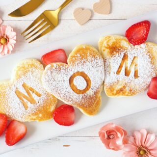 Mother's Day Gift: Heart shaped pancakes with MOM letters. Mothers Day breakfast concept. Top view table scene with a white wood background.