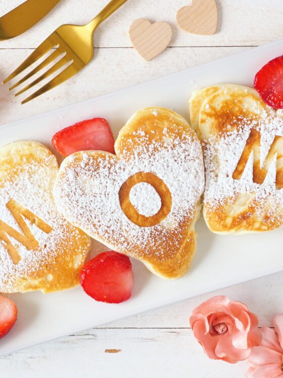 Mother's Day Gift: Heart shaped pancakes with MOM letters. Mothers Day breakfast concept. Top view table scene with a white wood background.