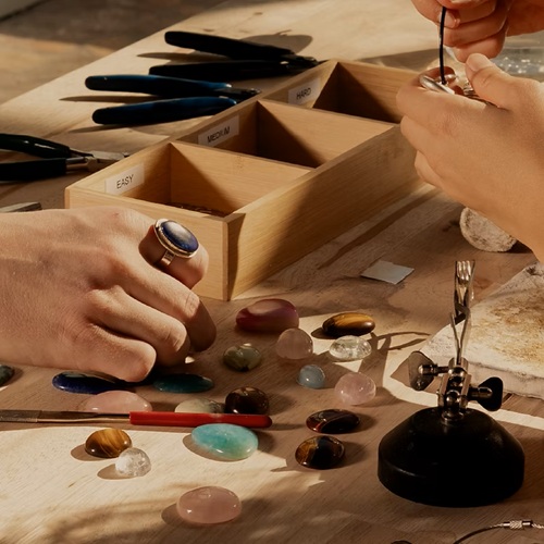 Mother's Day: pair of hands assembling jewelry with loose gems around