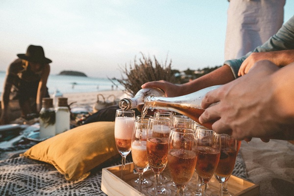 Sundowner: Beach party with person pouring sparkling wine