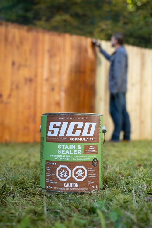 Wood Staining: Sico Formula 77 can in the foreground with a man staining a fence in the background