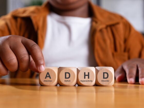 Fine Motor Skills in Kids with ADHD: Hand of black boy puts wooden cube with ADHD, Attention Deficit Hyperactivity Disorder on table.