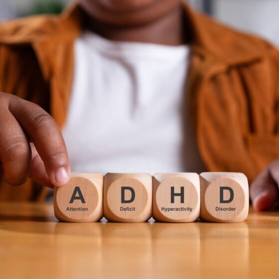 Fine Motor Skills in Kids with ADHD: Hand of black boy puts wooden cube with ADHD, Attention Deficit Hyperactivity Disorder on table.