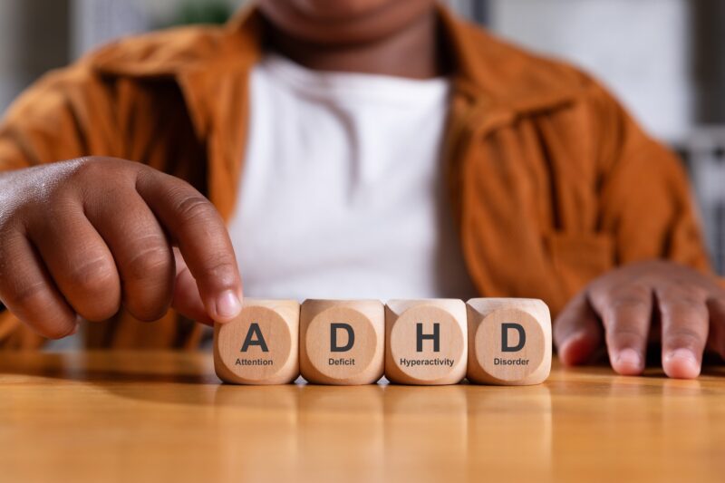 Fine Motor Skills in Kids with ADHD: Hand of black boy puts wooden cube with ADHD, Attention Deficit Hyperactivity Disorder on table.