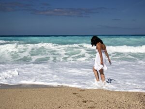 Wanting More: Woman walking in the surf on the beach in a white dress