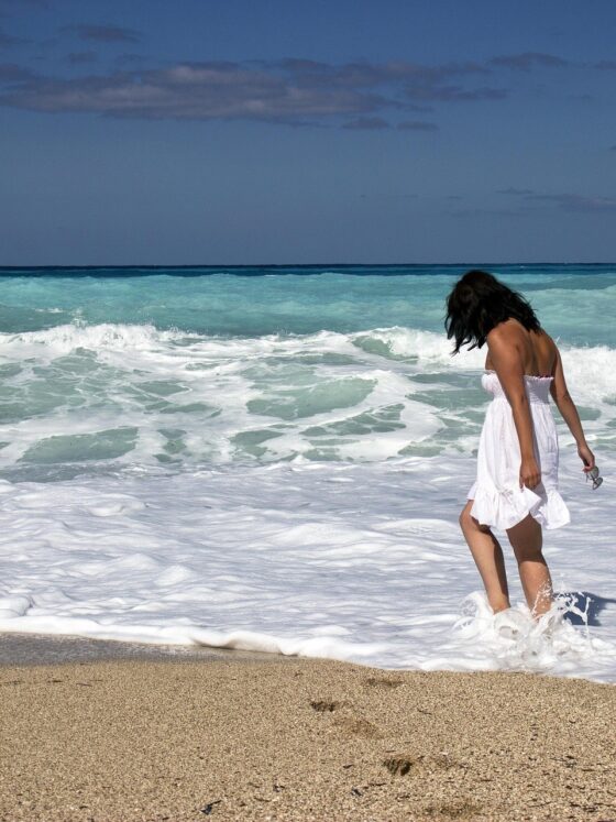 Wanting More: Woman walking in the surf on the beach in a white dress