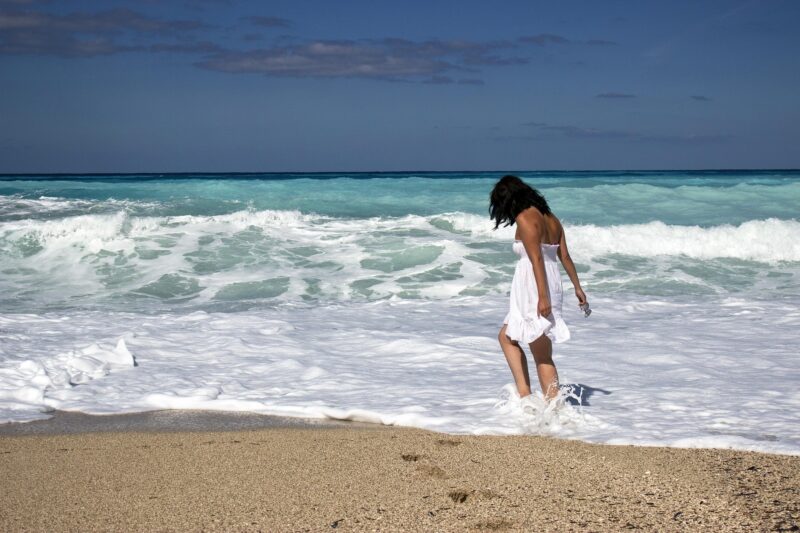 Wanting More: Woman walking in the surf on the beach in a white dress