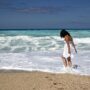 Wanting More: Woman walking in the surf on the beach in a white dress