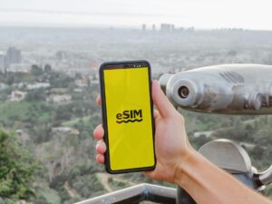 eSim: Hand holding a cell phone with eSim on the screen against a city view background