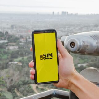 eSim: Hand holding a cell phone with eSim on the screen against a city view background
