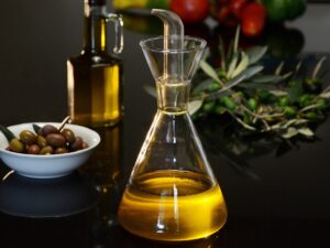 Eating Well: Olive oil bottle in the foreground with bowl of olives, rosemary and tomatoes in the background