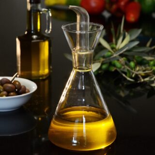 Eating Well: Olive oil bottle in the foreground with bowl of olives, rosemary and tomatoes in the background