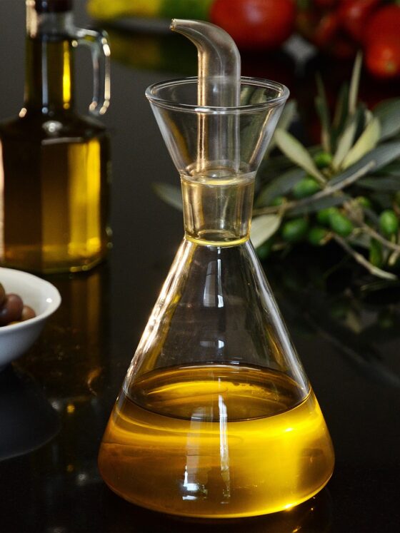 Eating Well: Olive oil bottle in the foreground with bowl of olives, rosemary and tomatoes in the background