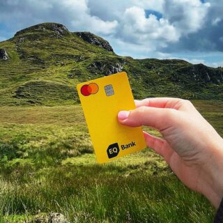 eq bank card: Woman's hand holding an EQ Bank Card in front of a hill