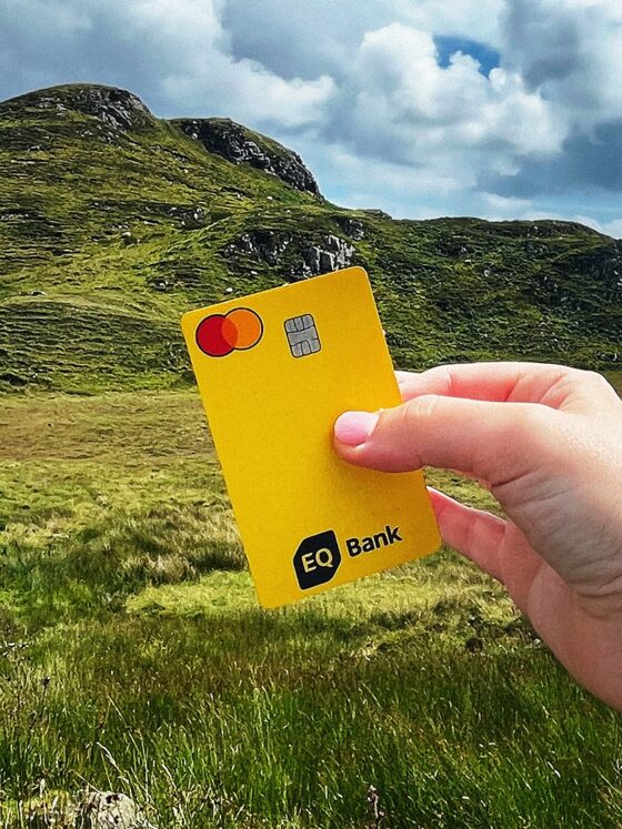 eq bank card: Woman's hand holding an EQ Bank Card in front of a hill