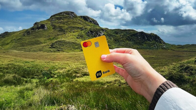 eq bank card: Woman's hand holding an EQ Bank Card in front of a hill