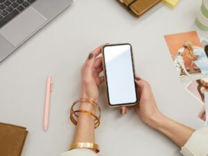 Digital Declutter: Woman's hand holding a smartphone in front of her laptop