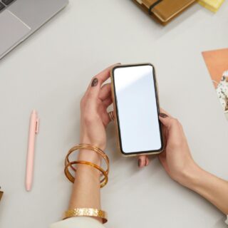 Digital Declutter: Woman's hand holding a smartphone in front of her laptop