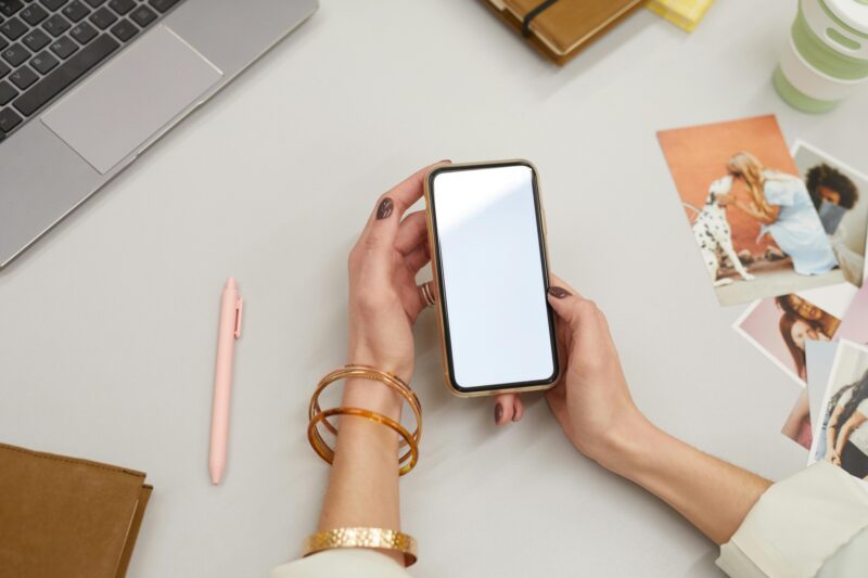 Digital Declutter: Woman's hand holding a smartphone in front of her laptop