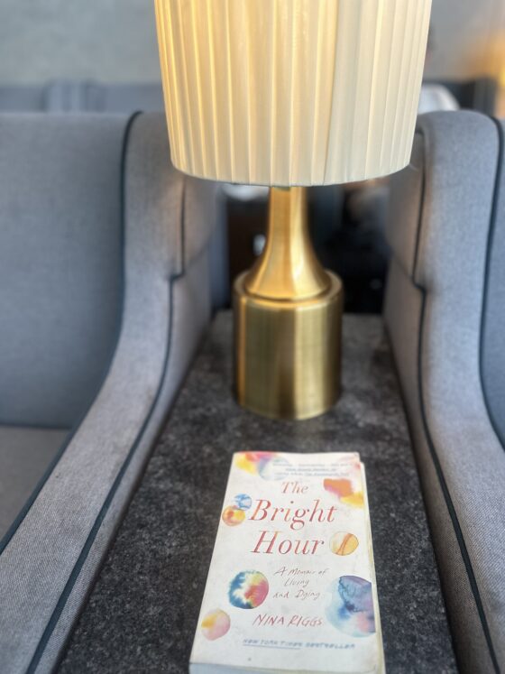 The Bright Hour: The book sitting on a table in the foreground with a brass lamp in the background between two chairs