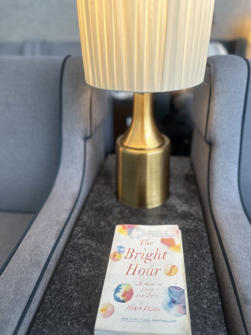 The Bright Hour: The book sitting on a table in the foreground with a brass lamp in the background between two chairs