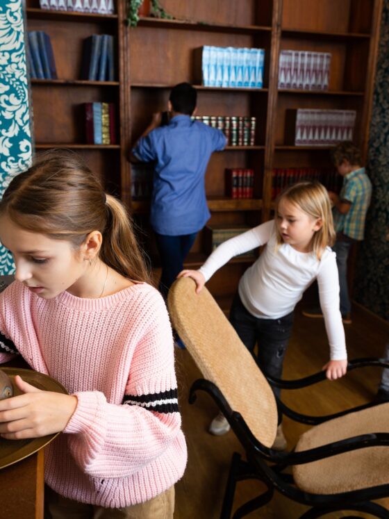 Escape Room: Interested tween girl examining ancient kettle in quest room stylized as old library