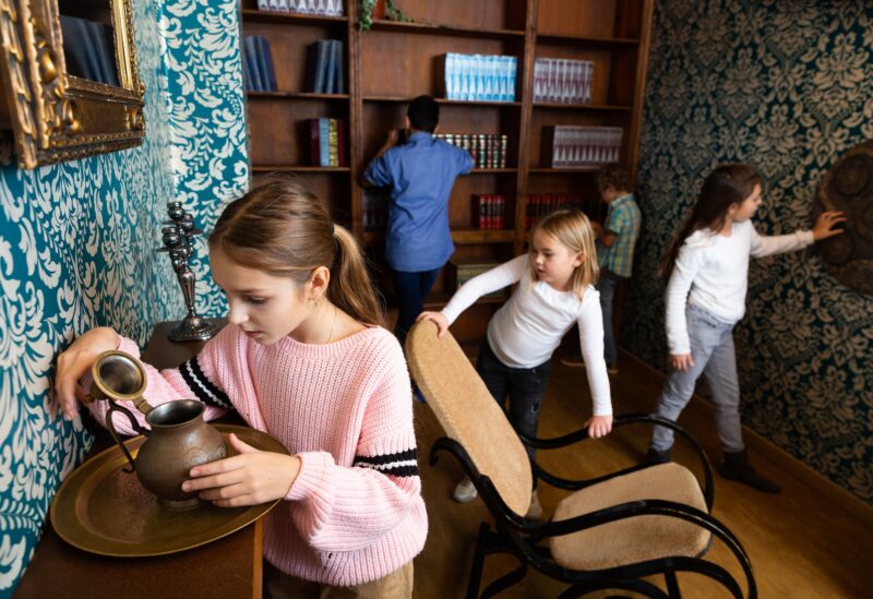 Escape Room: Interested tween girl examining ancient kettle in quest room stylized as old library