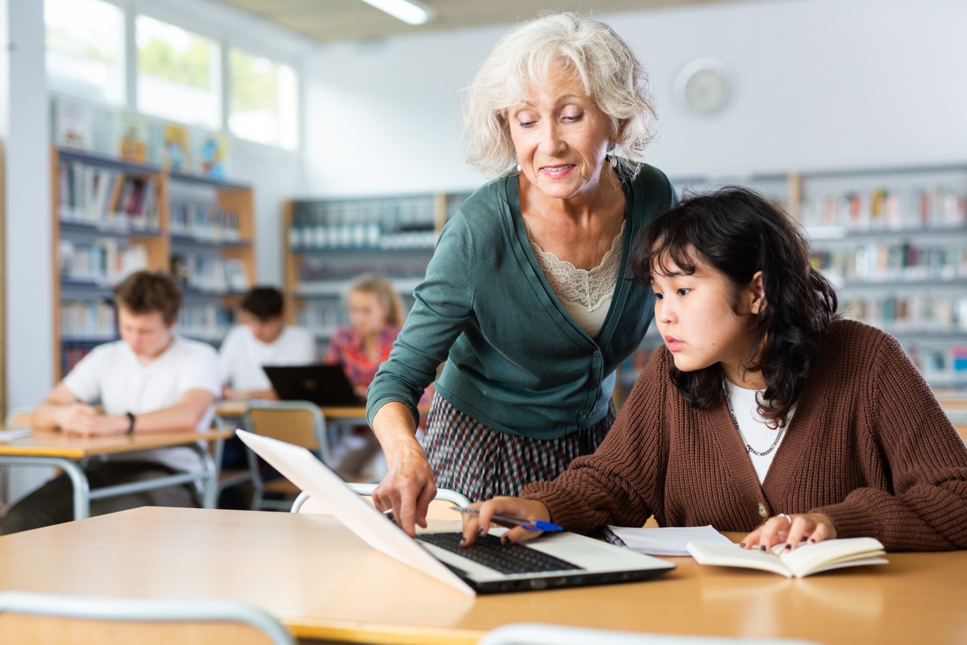 Volunteering: Elderly female teacher helps schoolgirl solve the equation in the school library