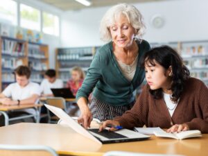 Volunteering: Elderly female teacher helps schoolgirl solve the equation in the school library