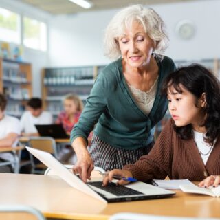Volunteering: Elderly female teacher helps schoolgirl solve the equation in the school library