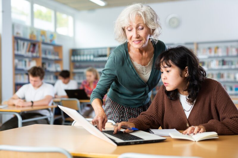 Volunteering: Elderly female teacher helps schoolgirl solve the equation in the school library