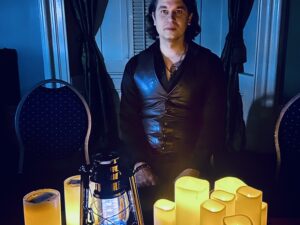 Beverley Street Séance RESURRECTION: Jaymes White in front of electric candles and lanterns