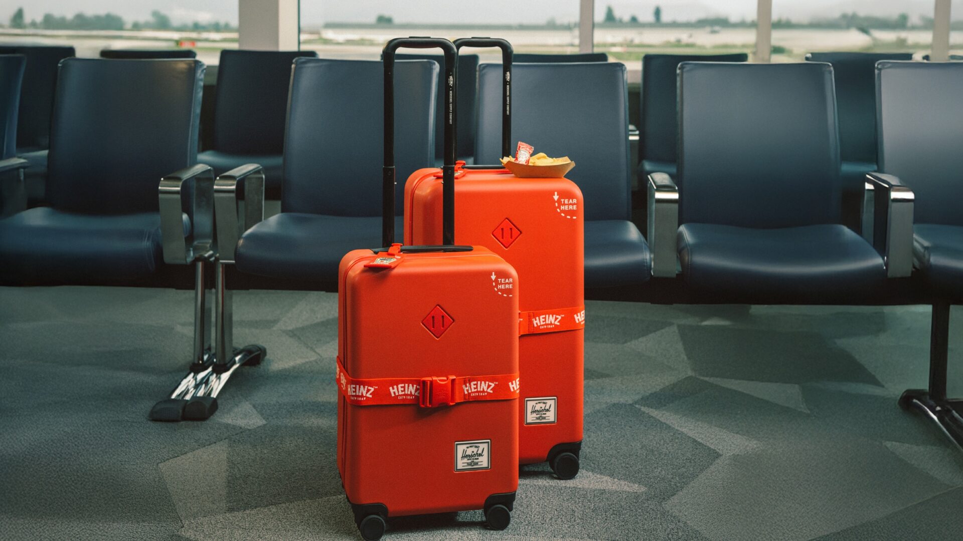 Herschel x HEINZ: Large and carry on red luggage in front of airport seats