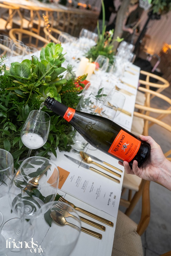 Prosecco: Hand holding a bottle of Prosecco as it's poured into a glass at an event dining table