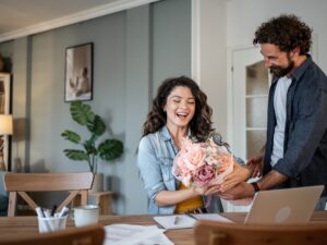 Busy Husband: adult man surprising his mid adult wife with a stunning bouquet of flowers while working from home, creating a heartwarming moment filled with love and appreciation