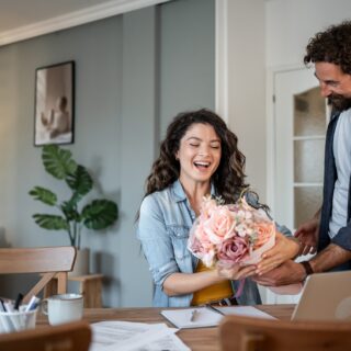 Busy Husband: adult man surprising his mid adult wife with a stunning bouquet of flowers while working from home, creating a heartwarming moment filled with love and appreciation
