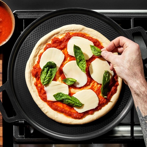 Man's hand adding basil to a pizza on a Hexclad Hybrid Pizza Steel