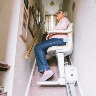 Stairlift: Senior woman using automatic stair lift on a staircase at her home.