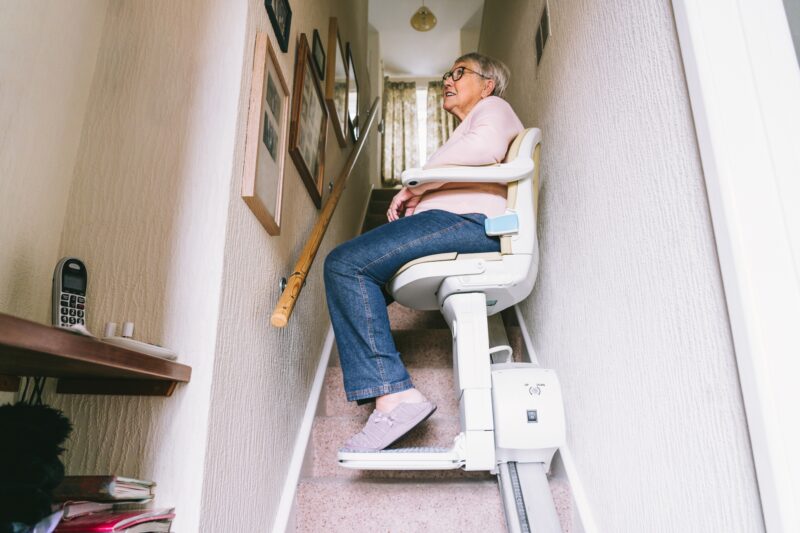 Stairlift: Senior woman using automatic stair lift on a staircase at her home.