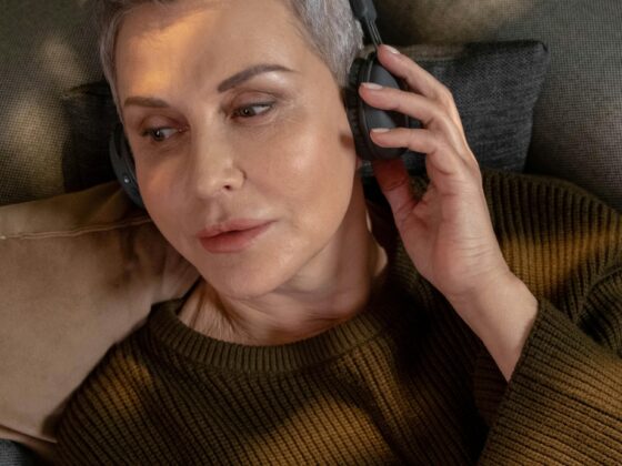 Music For Menopause: Woman in her 60s with short hair lying down with headphones on