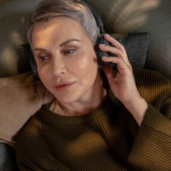 Music For Menopause: Woman in her 60s with short hair lying down with headphones on